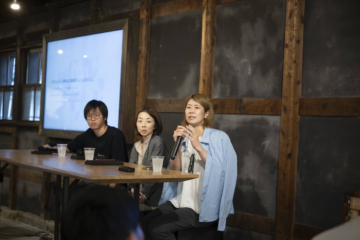 登壇者３名が観客の前で話している様子、横溝さんがマイクを握って話している